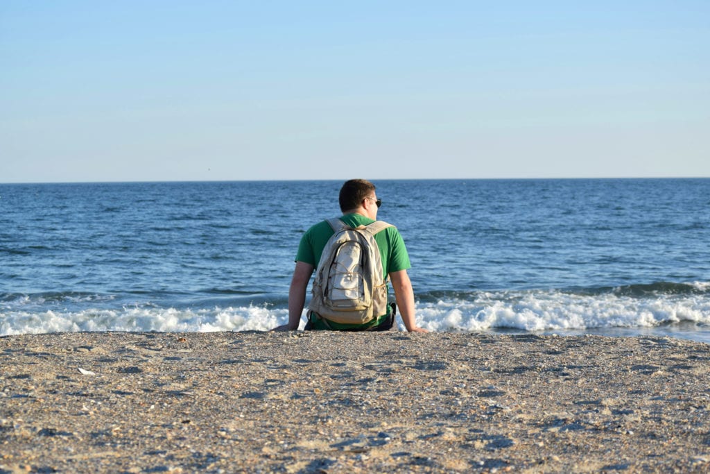 杰里米·斯道姆背着背包坐在北卡罗来纳州梅肯堡州立公园的海滩上俯瞰着大海