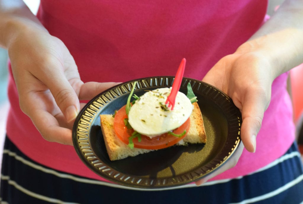凯特·斯道姆穿着粉红色衬衫，手里拿着一个盘子，上面有面包、西红柿和奶酪做成的小小吃。图为餐前小吃。