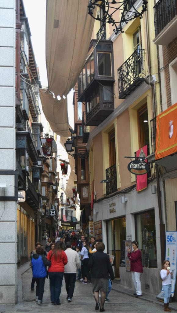西班牙托莱多的一条小街道，右边是一栋黄色建筑，下面是一群人