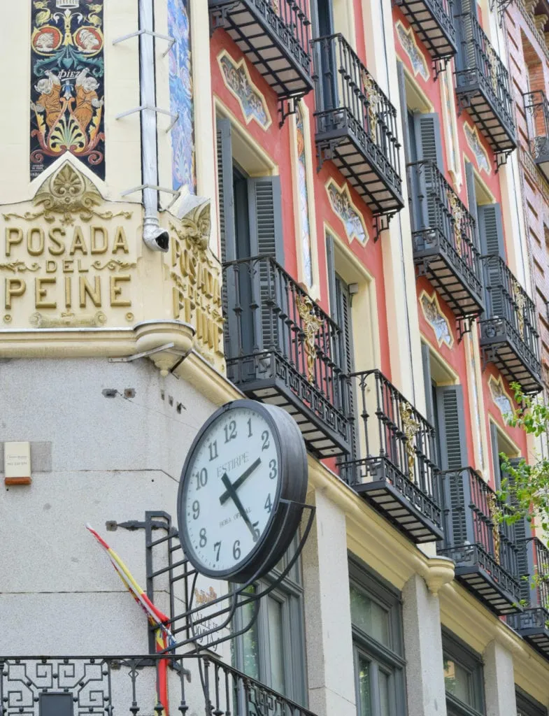 西班牙马德里一座红色建筑上的时钟，黑色锻铁阳台——在马德里的3天里，你会看到很多这样美丽的建筑!
