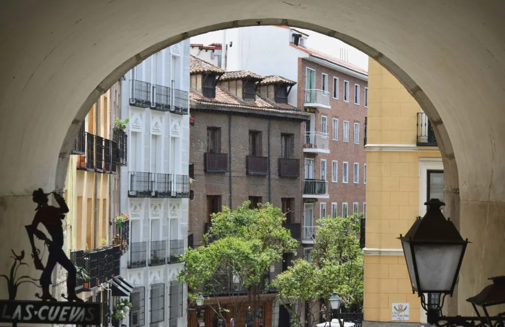 西班牙马德里的拱门照片，背景中可见彩色建筑