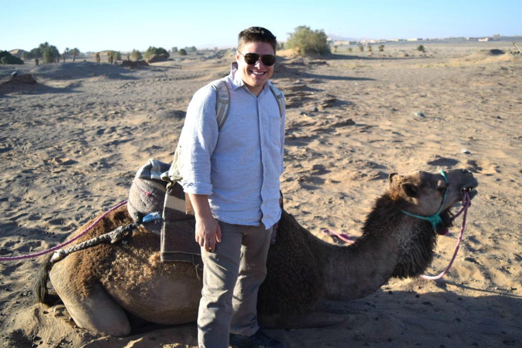 在摩洛哥沙漠里，杰里米·斯托姆站在一头骆驼前面