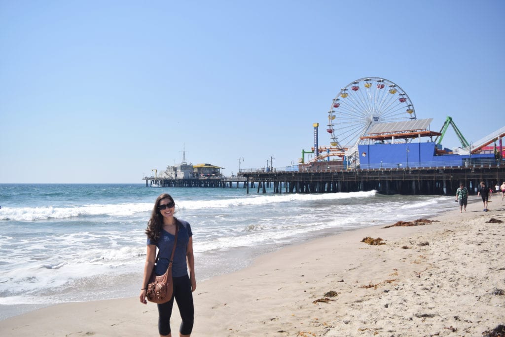 凯特·斯道姆站在加州洛杉矶圣莫尼卡码头旁边的海滩上，这是一些最经典的美国自驾游行程想法的最终目的地