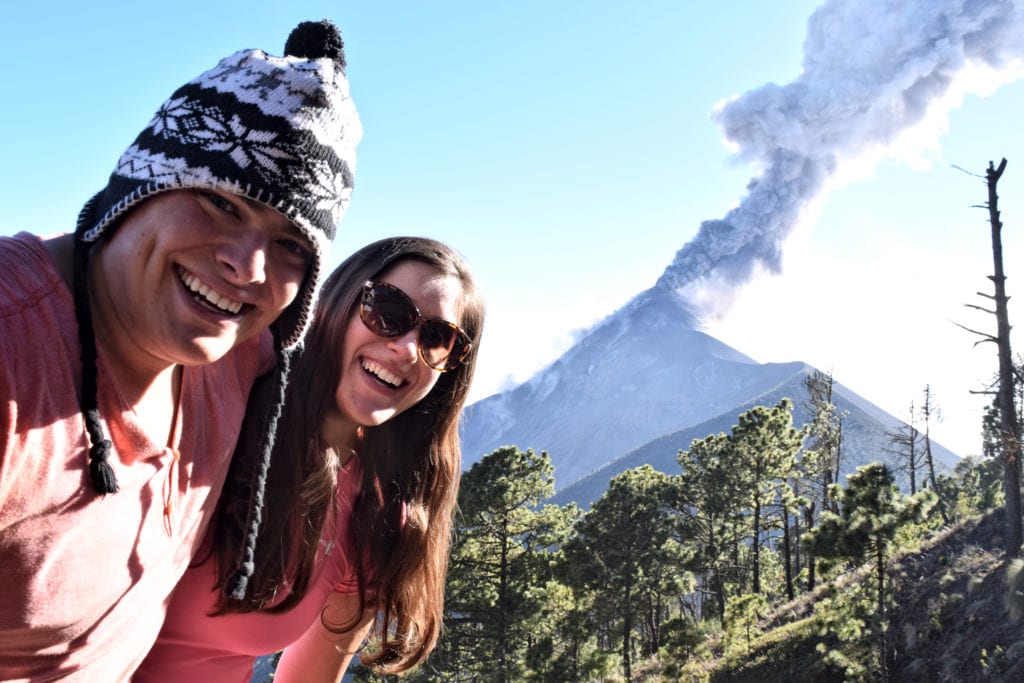 凯特和杰里米在阿卡特南戈火山前风暴，背景中的火山正在喷发