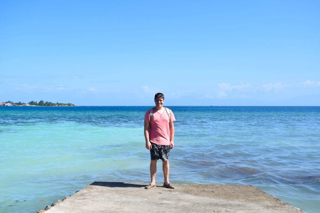 杰里米·斯托姆站在洪都拉斯乌利亚码头的尽头，俯瞰着水面，穿着短裤和t恤，典型的衣服是去中美洲墨西哥的装箱单上的