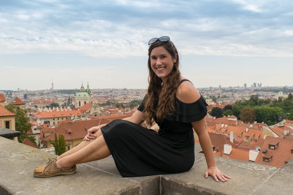 kate storm sitting on a ledge overlooking a free view of the prague skyline when traveling prague on a budget