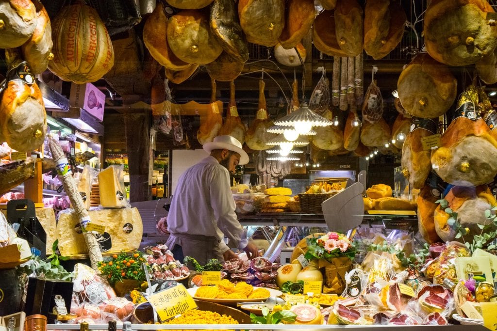 在意大利博洛尼亚，一名男子切割熟食，周围是展示的肉类