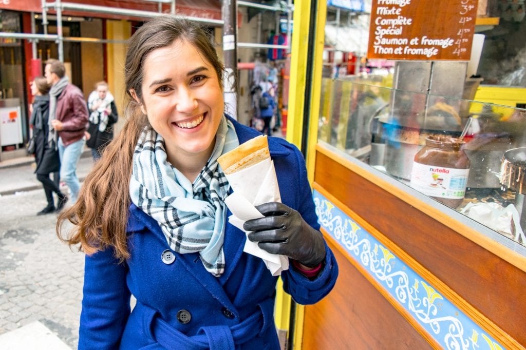 凯特·斯道姆身穿蓝色外套，手里拿着可丽饼在巴黎观光——任何去巴黎的周末旅行都至少需要吃两个可丽饼!
