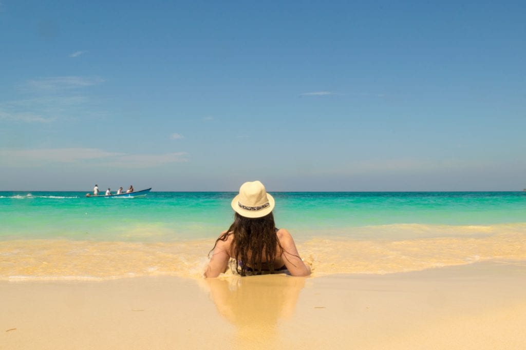 凯特·斯道姆戴着遮阳帽躺在卡塔赫纳附近的普拉亚布兰卡海滩上，看着大海。远处有一条船。