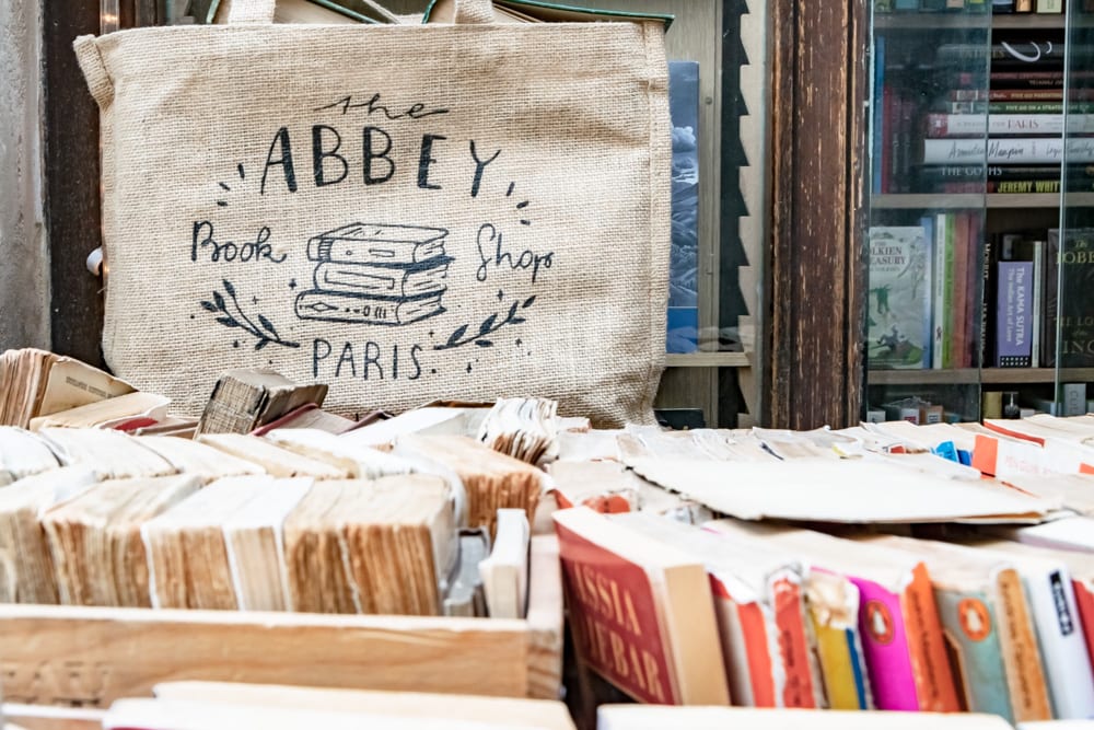Photo from Abbey Bookshop in Paris. There are the tops of spines of books visible in the foreground and a tote bag that says 