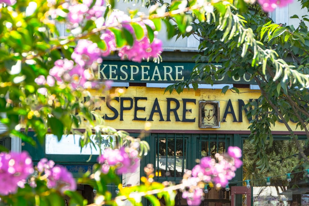 front facade of shakespeare and company as seen through blooming flowers during a travel paris itinerary