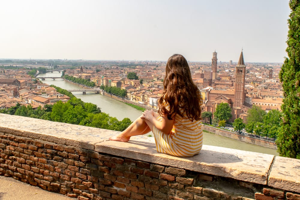 凯特穿着黄色连衣裙坐在圣彼得堡的墙上，俯瞰阿迪杰河和维罗纳的天际线。维罗纳是你在意大利度蜜月的好地方!