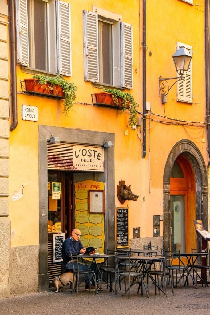 男人和狗坐在黄色建筑的意大利酒吧外，在酒吧喝咖啡是在意大利奥维多必做的事情之一