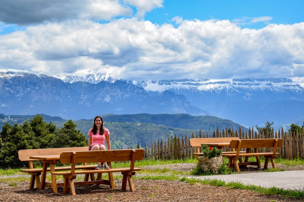 凯特·斯道姆在意大利公路旅行时，身穿粉色衬衫坐在多洛米蒂山脉的野餐桌上