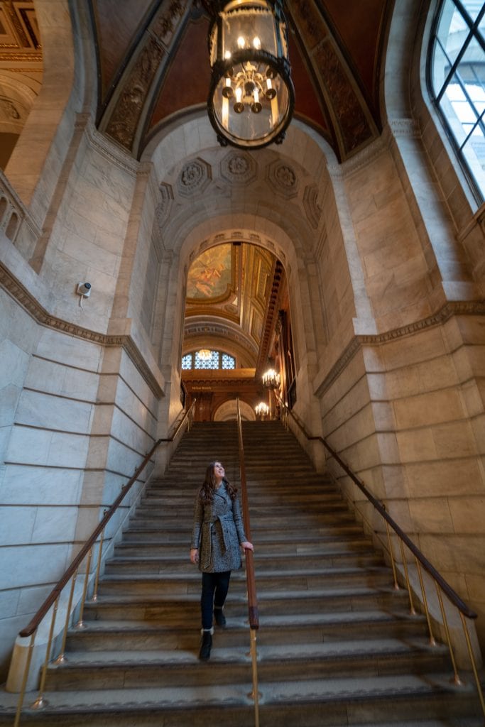凯特走下纽约公共图书馆第五大道分馆的石阶。凯特穿着一件灰色的外套。