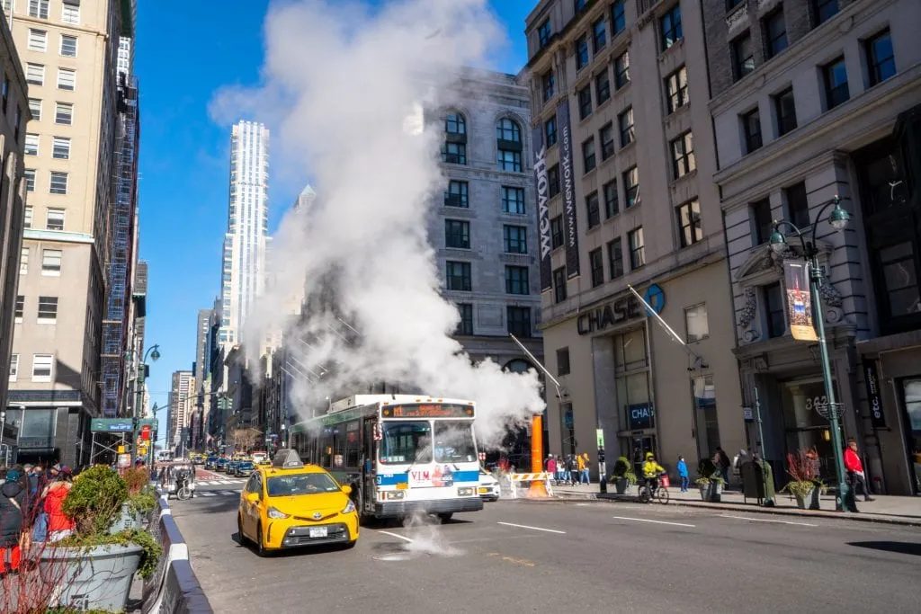 一辆出租车和一辆公共汽车驶过的纽约街道上的一个冒烟的壁炉