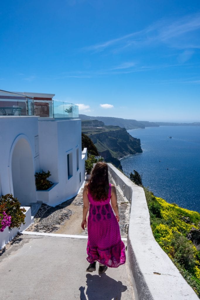 在希腊圣托里尼岛，凯特身穿粉色连衣裙穿过一个村庄