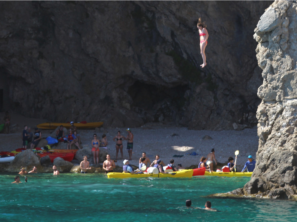 克罗地亚杜布罗夫尼克的女孩悬崖跳跃与其他游泳者和附近的皮划艇