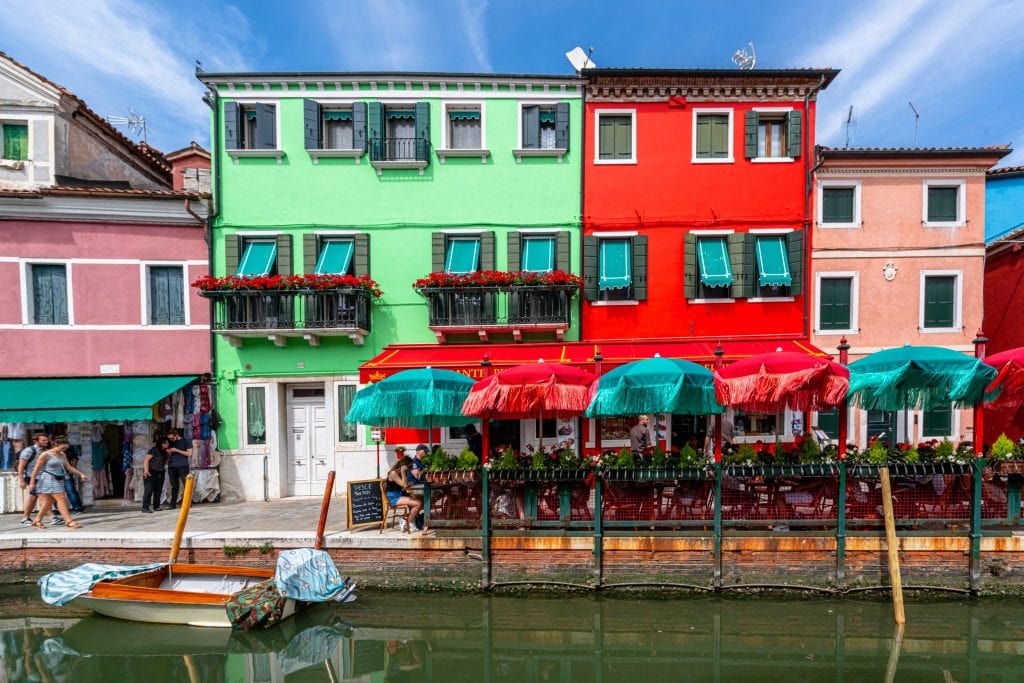 威尼斯五颜六色的房子的照片，前面有雨伞和运河。