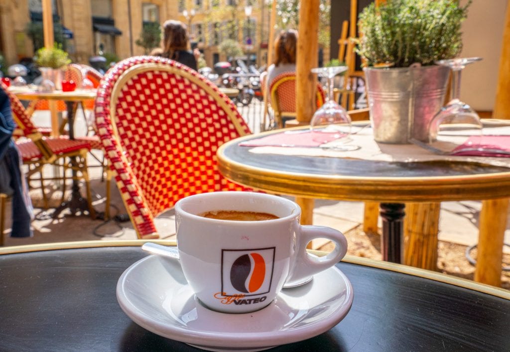在法国一个典型的法式早餐期间，一杯咖啡坐在户外的黑色桌子上，背景是一张红色的椅子
