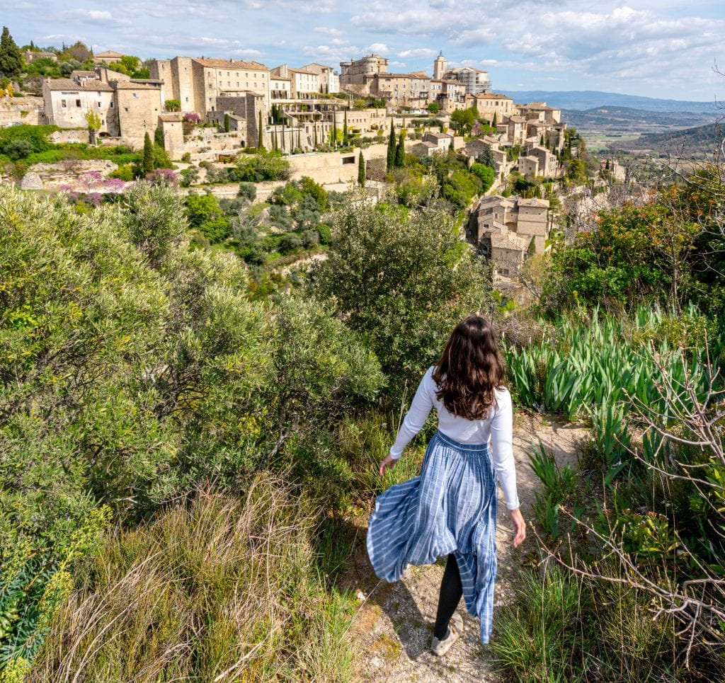 Kate in a blue skirt on a ledge overlooking Gordes, one of the best places to visit in the South of France