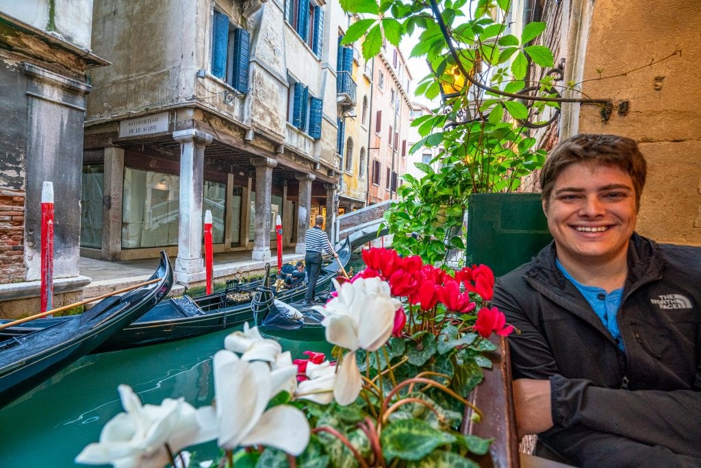 一个男人坐在威尼斯运河边的餐厅里。他旁边的橱窗里有个花盒。