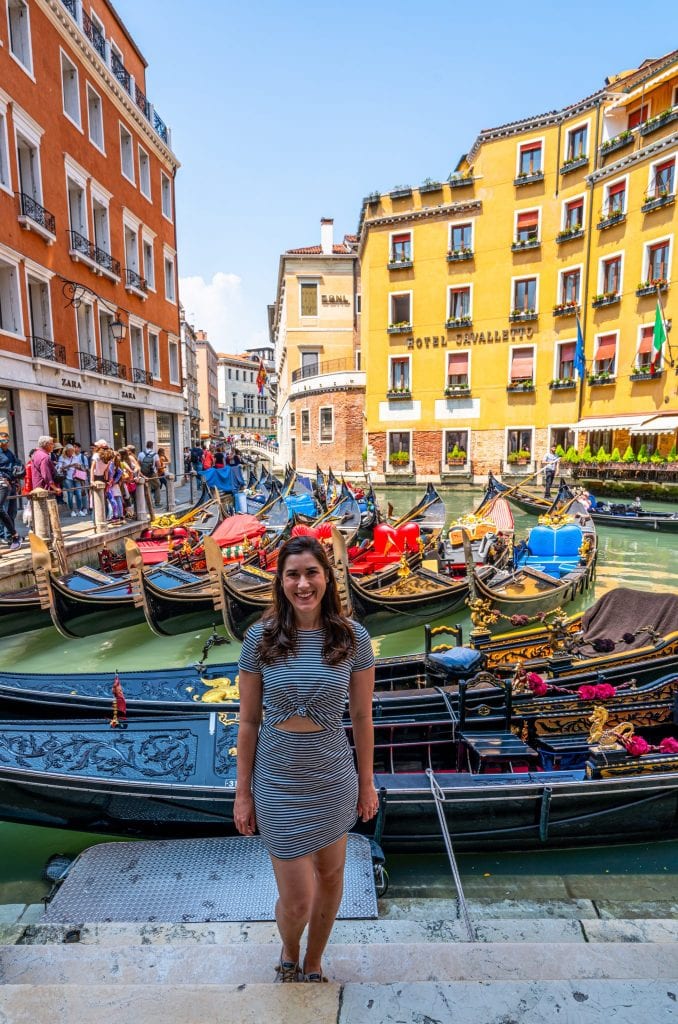身着条纹裙的凯特·斯道姆站在圣马可广场附近的一群贡多拉前，她身后是一座黄色的建筑——如果你想在威尼斯享受宁静的贡多拉之旅，这里可不是上车的最佳地点!