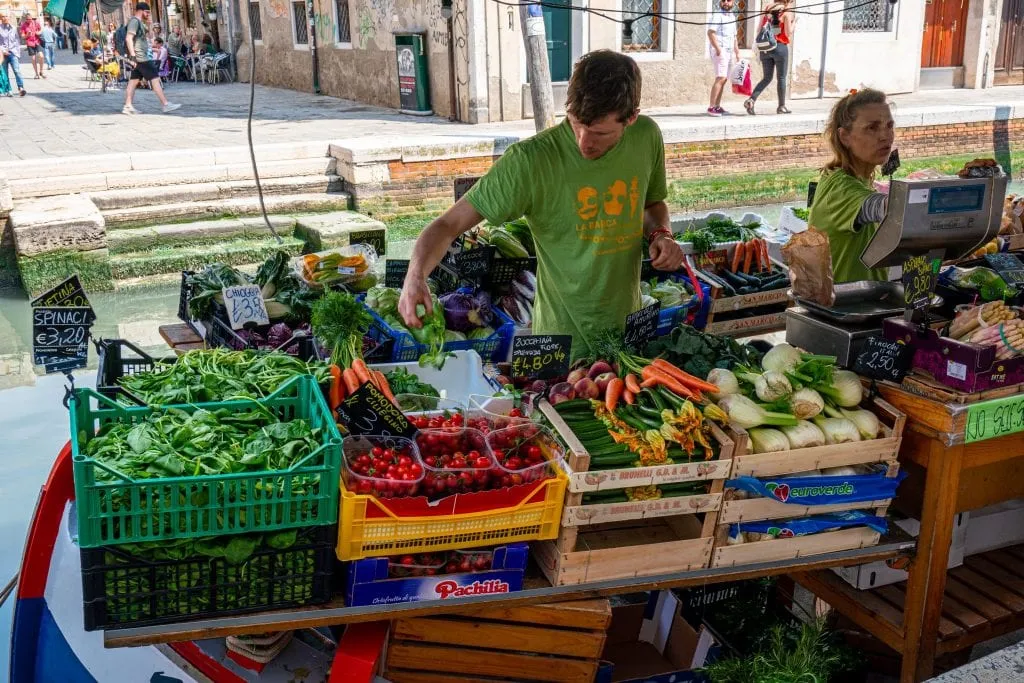 穿着绿色衬衫的男子在威尼斯dorsoduro蔬菜驳船上卖蔬菜