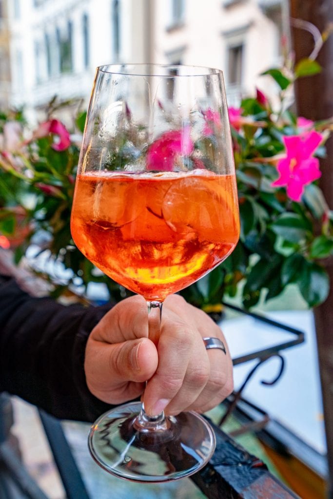 在威尼斯，在粉红色的花朵前被举着的Aperol Spritz的特写照片