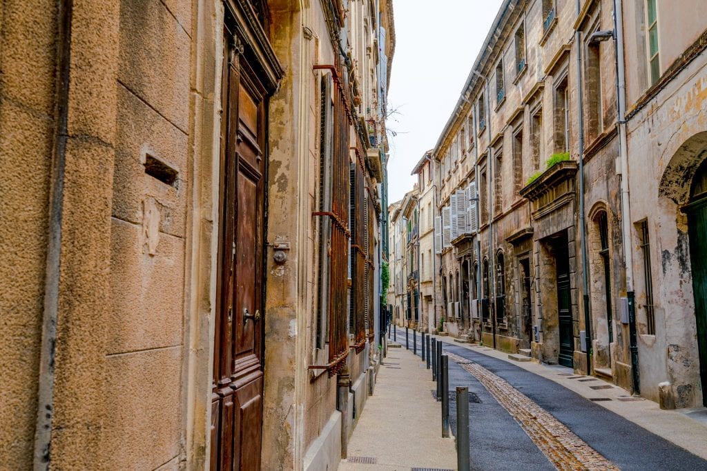 Photo of an empty street in Avignon, with brown buildings to either side. The road is curving to the left.