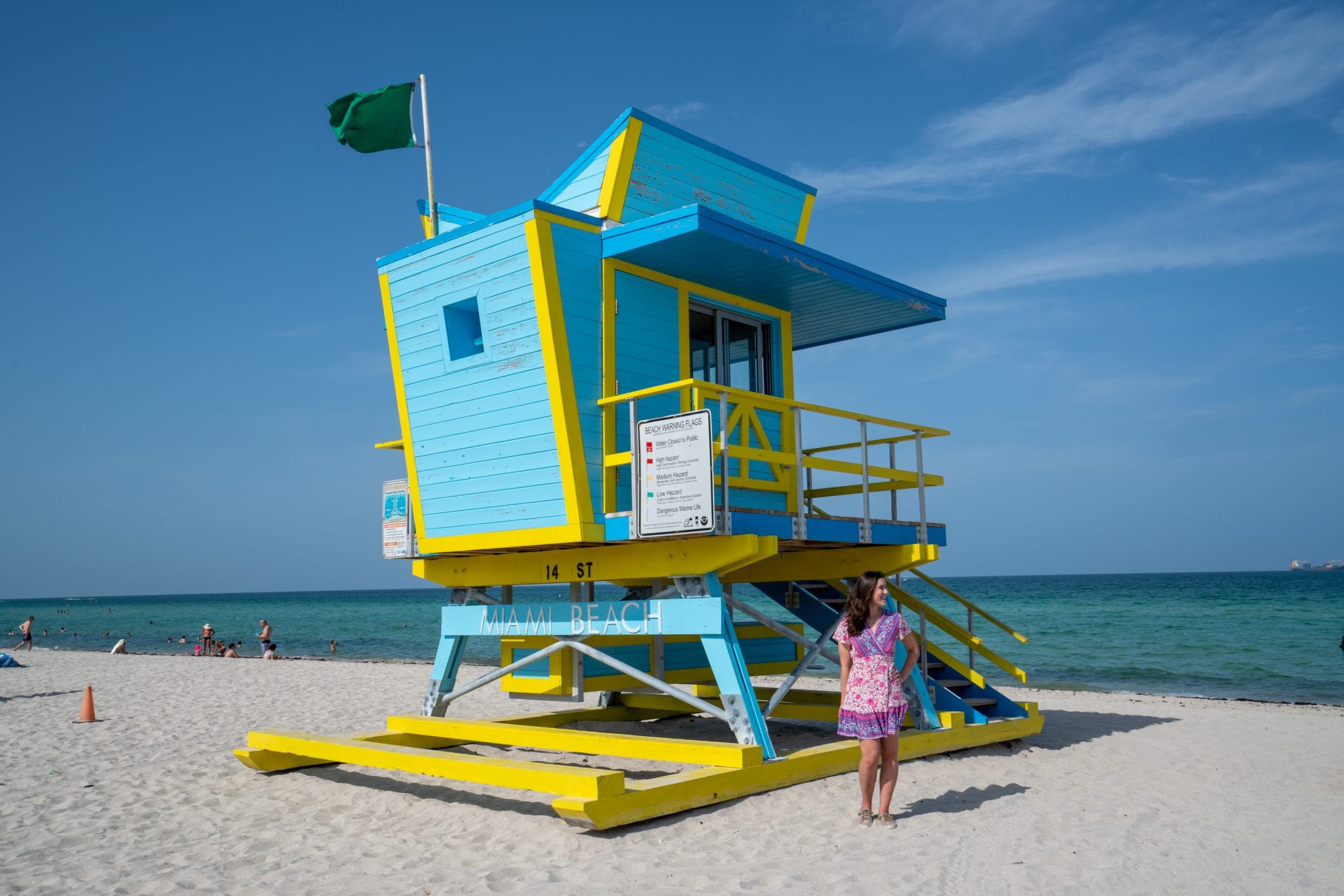 在迈阿密海滩的南海滩，凯特穿着粉红色的连衣裙站在一个蓝色装饰艺术的救生员站前。