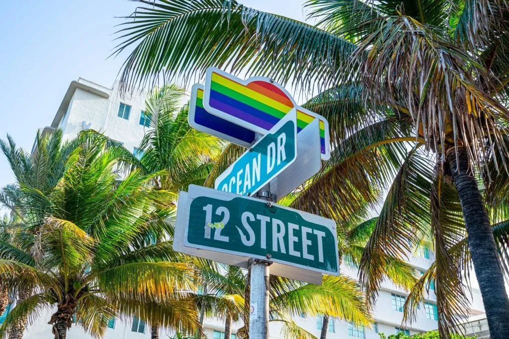 海径和第十二街的十字街标志照片。招牌上有骄傲的彩虹，背景是棕榈树。