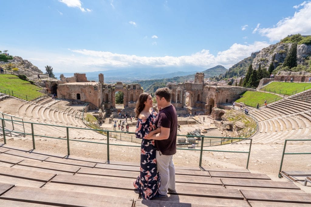 凯特和杰里米站在陶尔米纳的希腊剧院——参观这个地方是陶尔米纳最好的事情之一!凯特和杰里米面对面，凯特穿着一条碎花长裙。