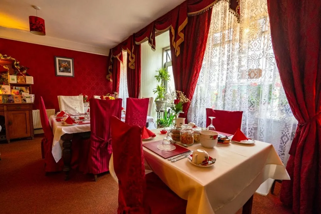 Inishross House的早餐室里有红色的椅子和红色的窗帘——绝对是你在爱尔兰度蜜月的一个舒适的地方!