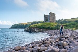 凯特·斯道姆站在爱尔兰丁格尔半岛的卵石滩上。密纳德城堡在她身后。这是在爱尔兰穿什么衣服的一个很好的例子!