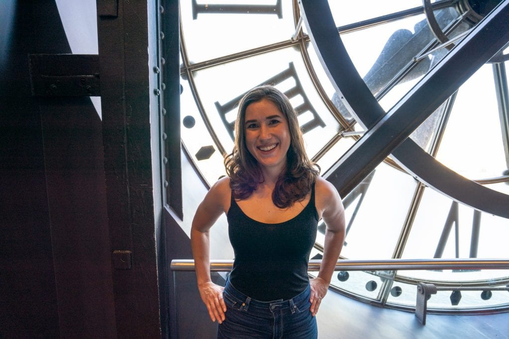 Kate Storm in a black tank stop standing in front of the clock in Musee d'Orsay, an excellent part of any 3 days in Paris France!