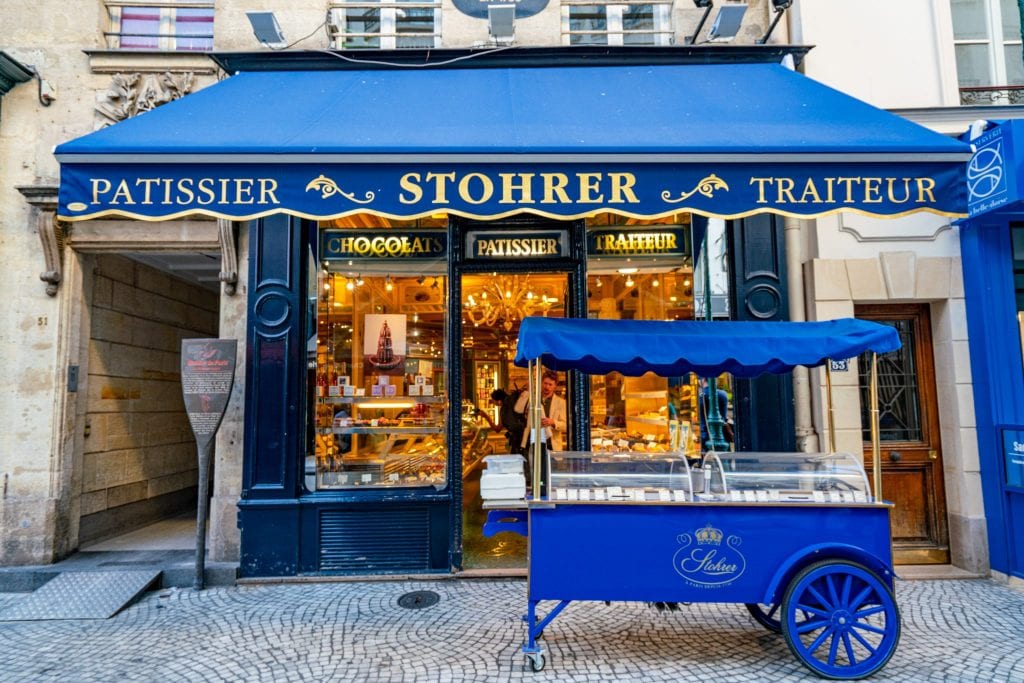 巴黎的Patisserie Stohrer的门面，蓝色的遮阳篷和蓝色的购物车在前面——当你在不走人迹的巴黎探索时，一定会在这里停下来。