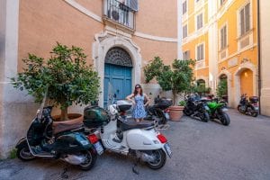 在意大利罗马的街道上，凯特·斯道姆穿着蓝色连衣裙站在一辆Vespa旁边——在罗马度假期间，你会看到很多这样的街道!