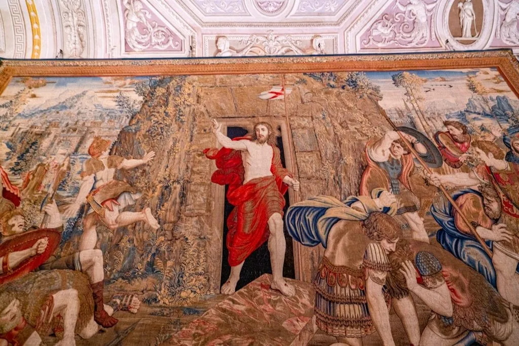 在罗马参观梵蒂冈博物馆时看到的挂毯上，前景是穿着红色长袍的耶稣