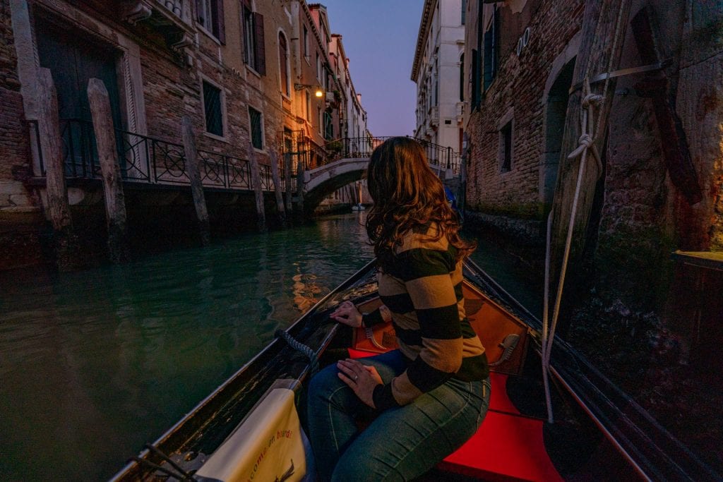 凯特·斯道姆(Kate Storm)晚上坐在贡多拉上，目光远离镜头。夜间乘坐贡多拉是威尼斯夜晚最值得做的事情之一!
