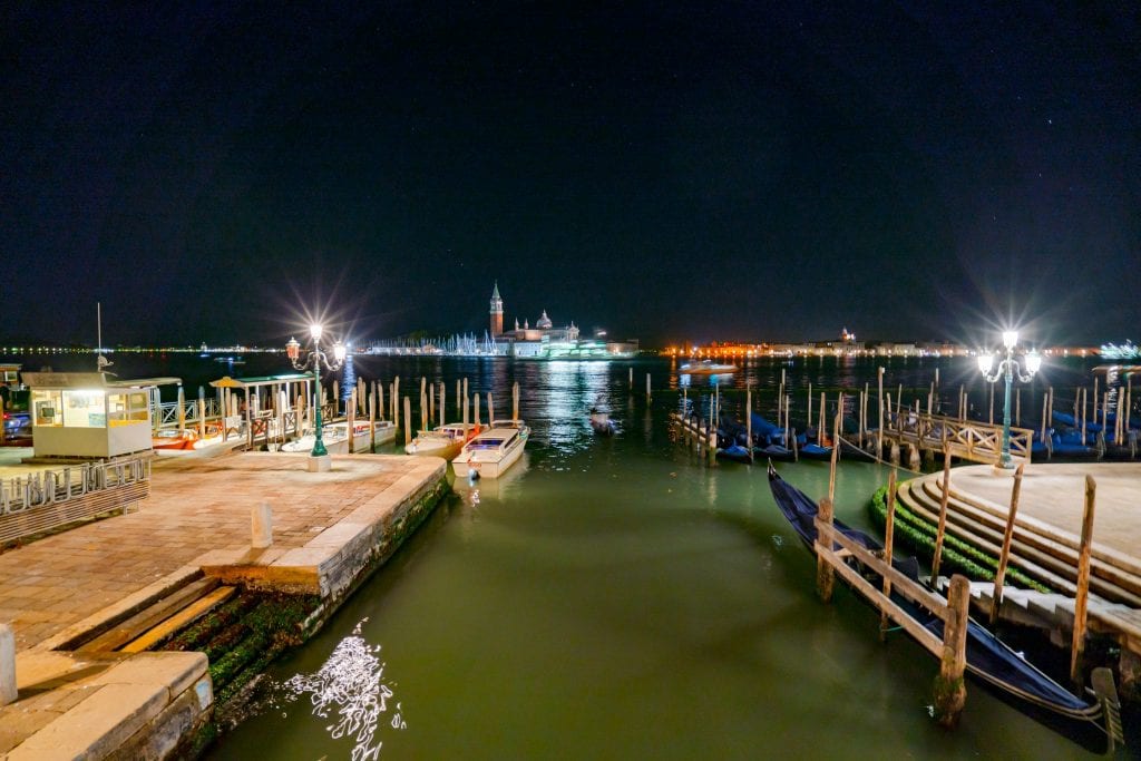从Riva degli Schiavoni拍摄的威尼斯泻湖的夜晚照片，可以看到停放的贡多拉——当决定晚上在威尼斯做什么时，不要忘记散步的乐趣!