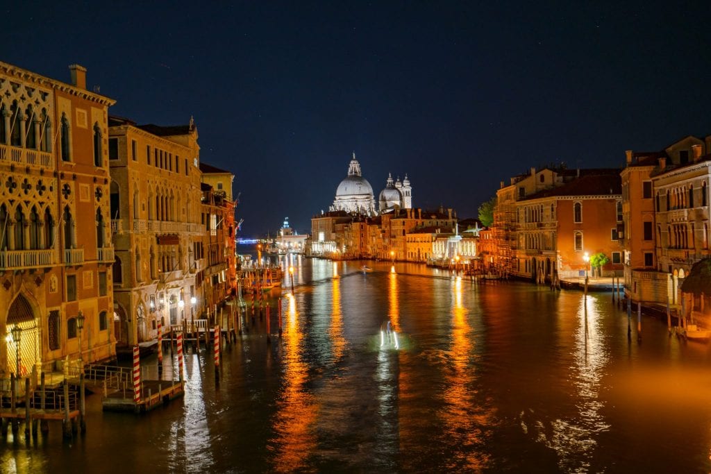 夜晚威尼斯大运河的照片，灯光倒映在水面上——当你决定晚上在威尼斯做什么时，一定要考虑到这样的风景。