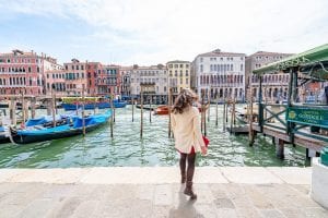 凯特·斯道姆背对着镜头站在大运河上，这是从佛罗伦萨到威尼斯一日游的必看景点!贡多拉停在运河边，凯特穿着一件奶油色毛衣。