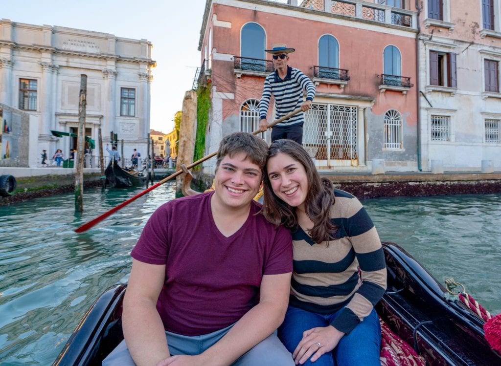 一对情侣坐在威尼斯的贡多拉上，身后可以看到船夫