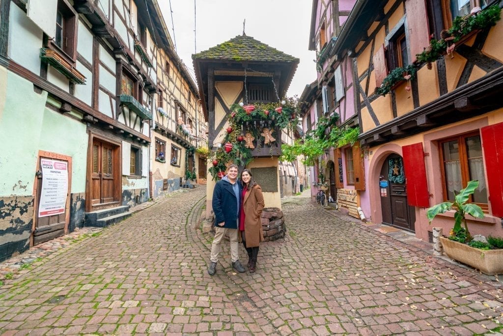 凯特·斯道姆和杰里米·斯道姆穿着外套站在法国埃吉斯海姆，周围是半木结构的房子