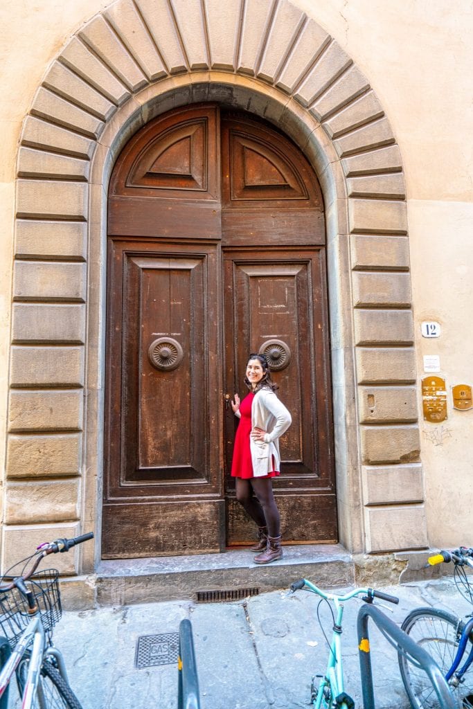 凯特·斯道姆穿着红色连衣裙走进佛罗伦萨的一扇大木门