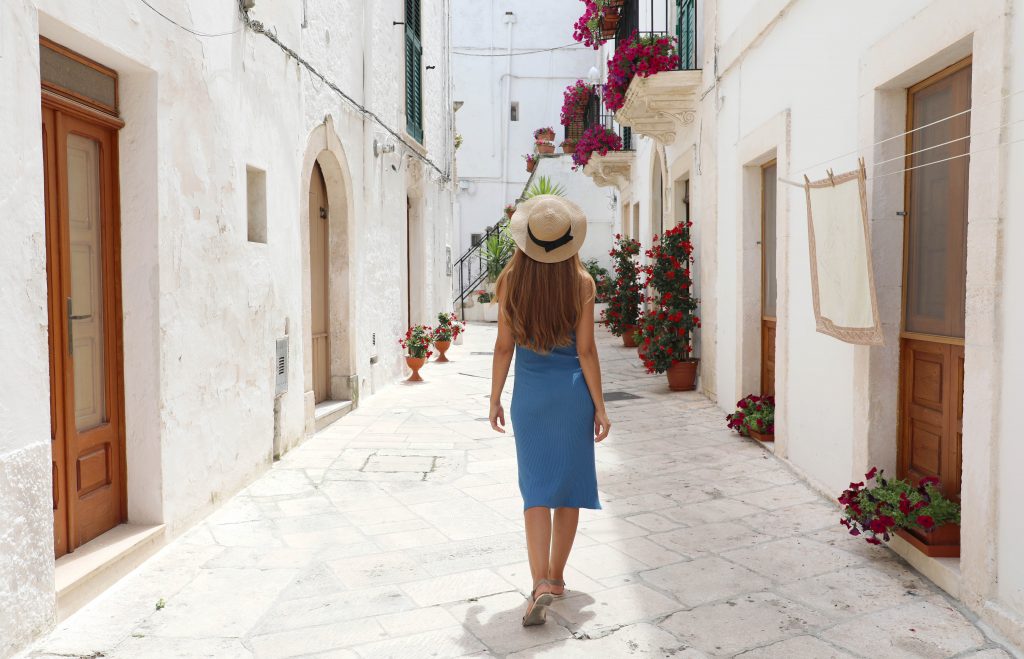 一位穿着蓝色连衣裙的年轻女子走在洛克罗通多的白色街道上，洛克罗通多是意大利最好的村庄之一