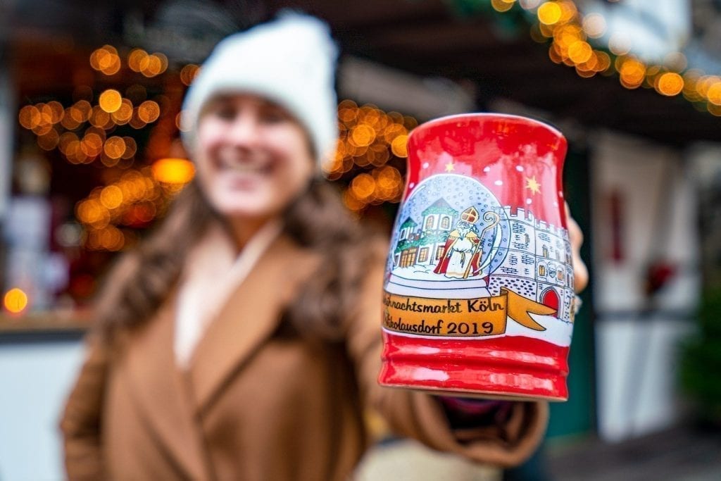 在科隆圣诞市场上，凯特·斯道姆拿着一个红色的马克杯对着镜头。科隆圣诞市场是欧洲最好的圣诞市场之一