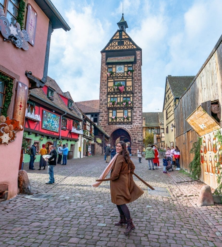 Kate Storm spinning in front of a clock tower in Riquewihr, one of the best day trips in Alsace!