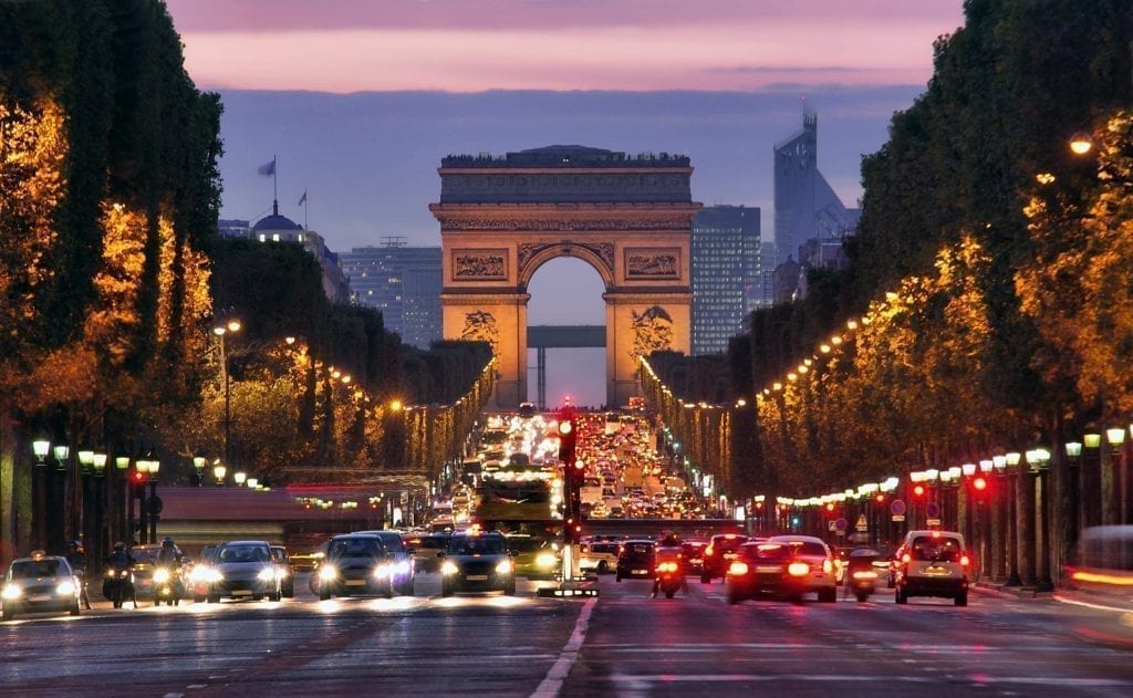 巴黎晚上的香榭丽舍大街，前面是车流，凯旋门在后面，可以看到轻微的粉色日落。